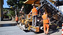 Eine spezielle Konstruktion am Straßenfertiger streut das Abstreumaterial für den Hightech-Asphalt (Mitte unten) auf den heißen Asphalt ...