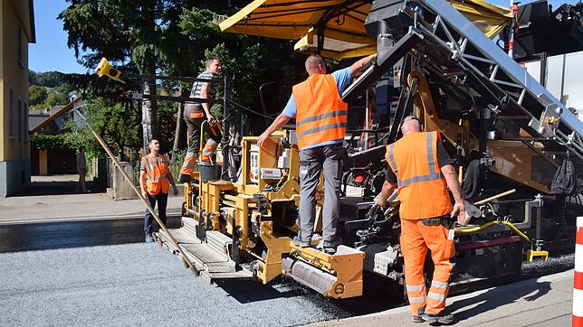 Eine spezielle Konstruktion am Straßenfertiger streut das Abstreumaterial für den Hightech-Asphalt (Mitte unten) auf den heißen Asphalt ...