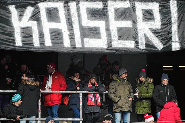 Besucher warten auf einer Tribüne. Transparente erinnern an den Kaiser.