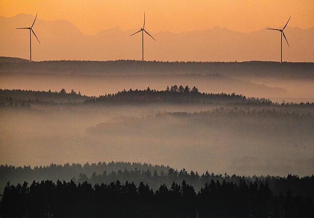 Windräder werden auf der Schwäbischen Alb am Morgen durch die aufgehende Sonne angestrahlt, während im Hintergrund durch die ...