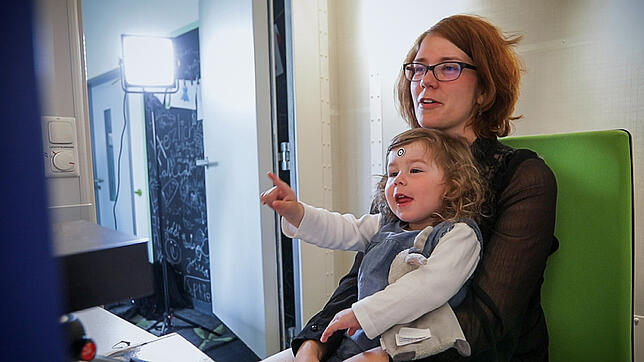 Die zweijährige Tochter Henriette sitzt im Labor auf dem Schoß ihrer Mutter.