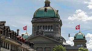 Die Schweizer Nationalfahne weht auf den kleinen Kuppeln auf dem Bundeshaus, dem Parlament, in Bern.