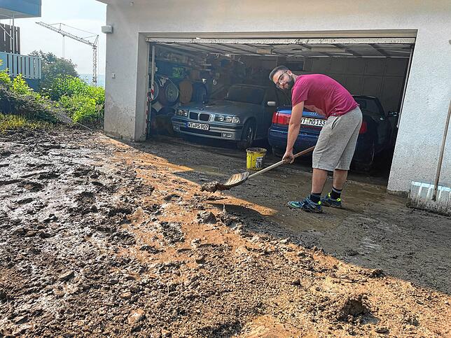 Pius Speicher versucht, den Schlamm nach den heftigen Regenfällen auf seinem Grundstück zu beseitigen.