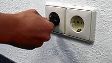 Eine Frau steckt einen Stecker in eine Steckdose: Stromversorgung ist heutzutage eine Selbstverständlichkeit. Stromausfälle können ...