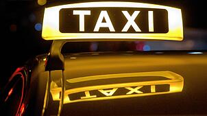 Ein Taxi-Schild leuchtet in der Nacht auf einem Fahrzeug.