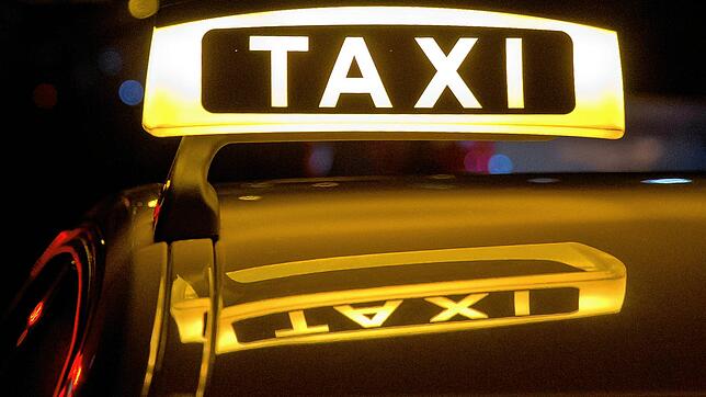 Ein Taxi-Schild leuchtet in der Nacht auf einem Fahrzeug.