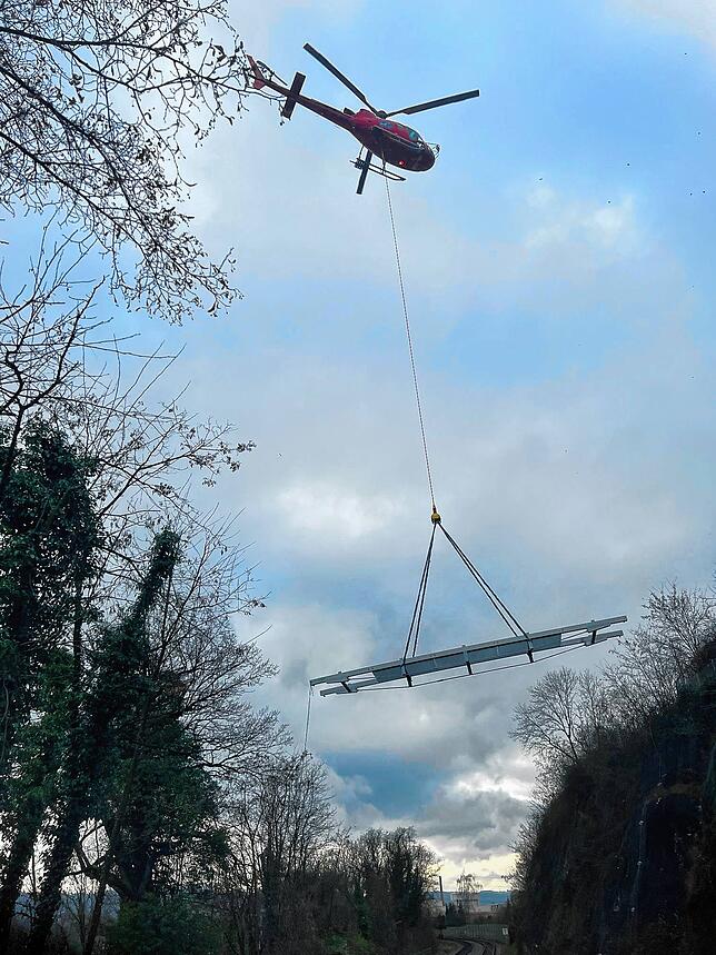 Der Helikopter transportiert den 10 Meter langen festen Steg über der Bahnlinie heran.