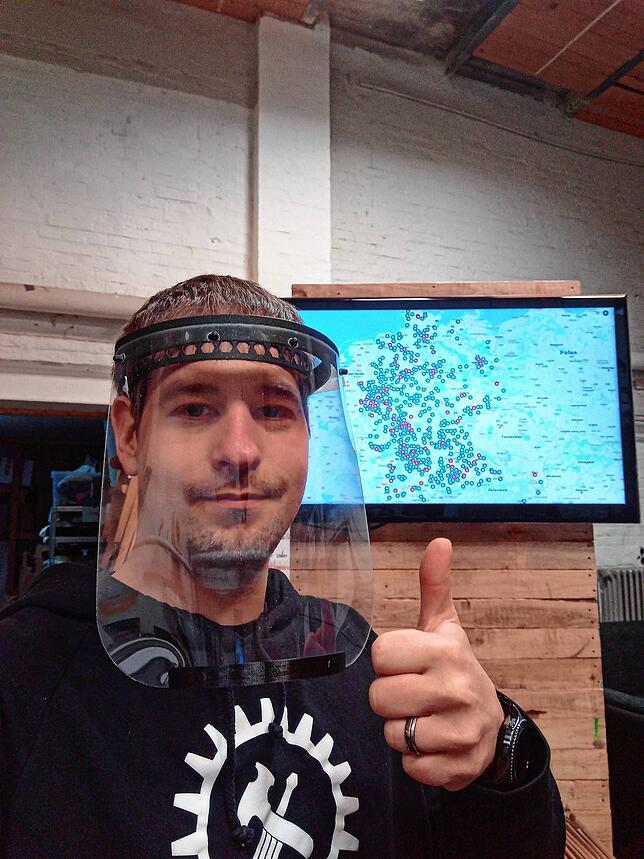 Dominik Hense vom Hammertime Kassel, Initiator von MakerVsVirus.org, mit einem fertigen Faceshield vor der Übersichtskarte der ...