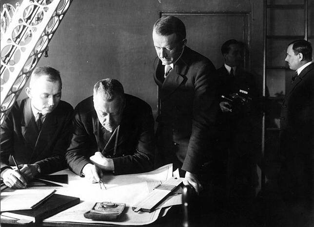 Hugo Eckener (2. von links), Kapitän von LZ 126, steckt mit den Zirkel auf einer Landkarte den Kurs ab. Links und rechts Offiziere ...
