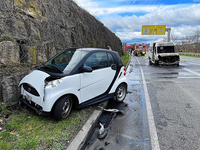 Ein Kleinwagen ist bei dem Unfall beschädigt worden. Im Hintergrund der ausgebrannte Transporter.
