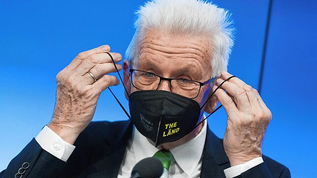 Winfried Kretschmann setzt sich nach einer Regierungs-Pressekonferenz im Landtag von Baden-Württemberg eine Schutzmaske auf.