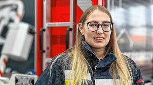 Janet Schüle (26) in Feuerwehrkleidung vor einem Einsatzfahrzeug.