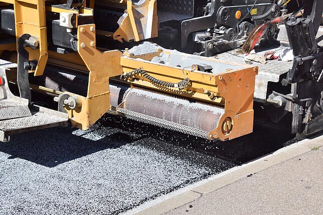Hier wird das spezielle Granulat auf den heißen Asphalt getreut.
