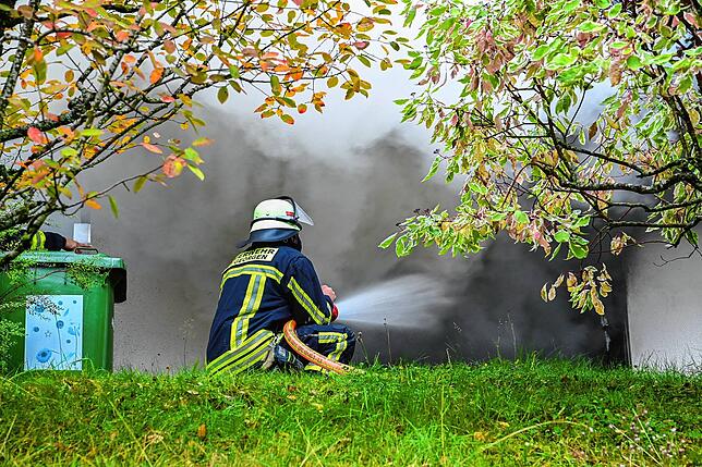 Ein Feuerwehrmann spritzt mit einem Strahlrohr Wasser in den brennenden Raum.