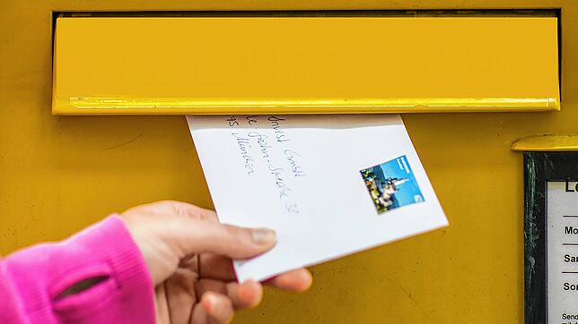 Eine Frau wirft einen Brief in einen Briefkasten. (Symbolbild)