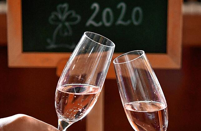 Ein Paar stößt vor einer Tafel, an der &ldquo;2020&bdquo; steht, mit Sektgläsern an.