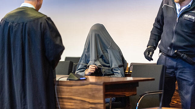 Christian L. sitzt mit einer Jacke über dem Kopf zu Prozessbeginn im Saal des Landgerichts Freiburg. Der frühere Betreuer von ...