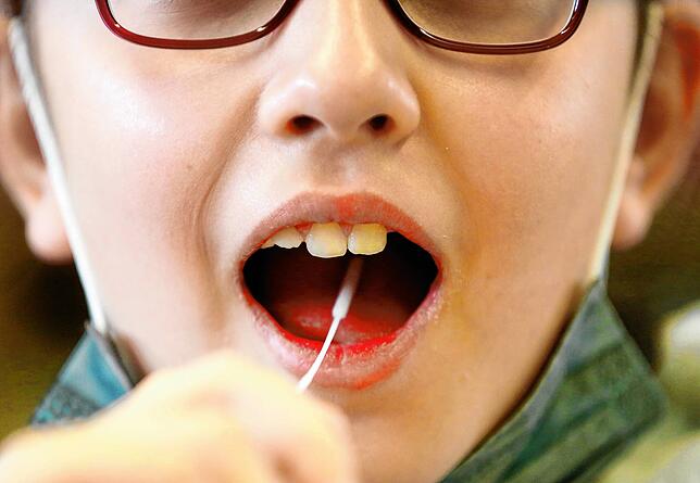 Ein Kind macht den so genannten Lolli-Test. Dabei wird ein Abstrich aus dem Rachen genommen. Gerade für kleine Kinder sind diese ...