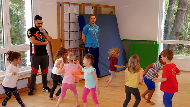 Erzieher Amin Hilali vom Kinderhaus am Rhein (links) und HSG-Trainer Kai Mittendorf lassen die Sportgarten-Kinder &bdquo;Zauberer und ...