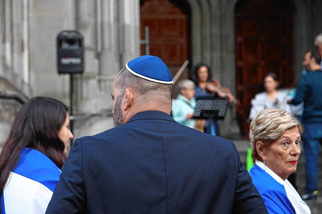 Ein Demonstrant jüdischen Glaubens trägt eine Kippa, andere haben sich die Flaggen mit den Farben Israels umgebunden.