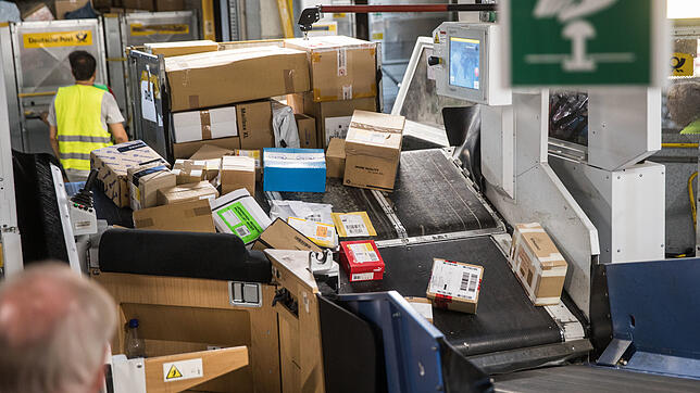 Mitarbeiter eines Paketzentrums der Deutschen Post verfrachten angelieferte Pakete auf Transportbänder. Auch die vielen Retouren tragen ...