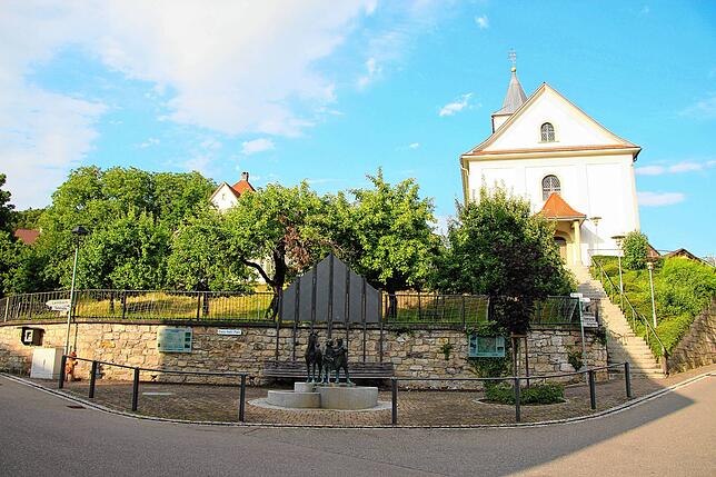 Der Martinsbrunnen am Franz-Kehl-Platz in der Dorfmitte, im Hintergrund die St. Martinskirche.