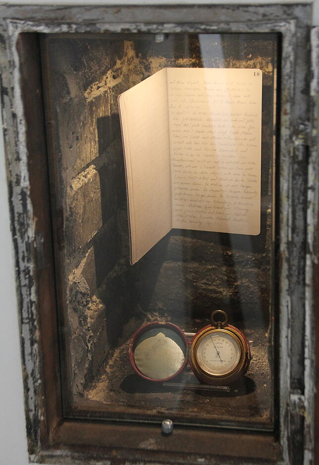 Die Nische zum ehemaligen Kamin ist ein Ausstellungskasten. Darin liegen ein Höhenmesser und das Expeditions-Tagebuch mit Seiten aus ...