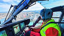 Ein Pilot der Schweizer Rega fliegt in dem neuen Rettungshelikopter über Basel. Im Hintergrund sieht man die Roche-Türme und den Rhein.