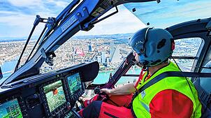 Ein Pilot der Schweizer Rega fliegt in dem neuen Rettungshelikopter über Basel. Im Hintergrund sieht man die Roche-Türme und den Rhein.