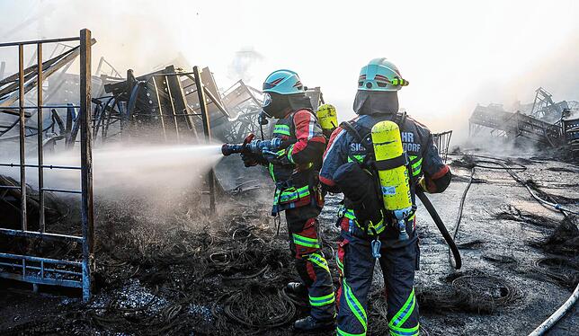 Einsatzkräfte der Feuerwehr löschen während eines Großbrandes auf dem Gelände eines Reifengroßhändlers brennende Reifen.