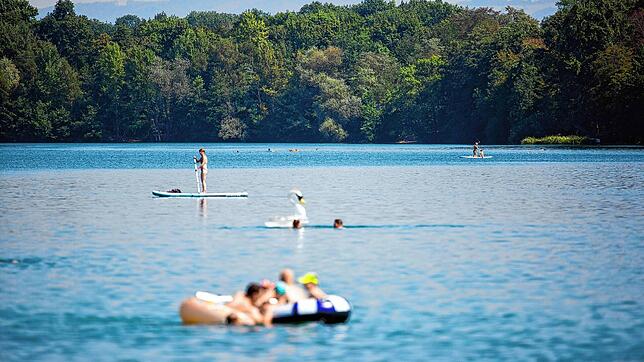 Eine Frau fährt auf einem Stand Up Paddle-Board über den Opfinger See und Badegäste baden im Wasser. In einem Freiburger Badesee soll ...
