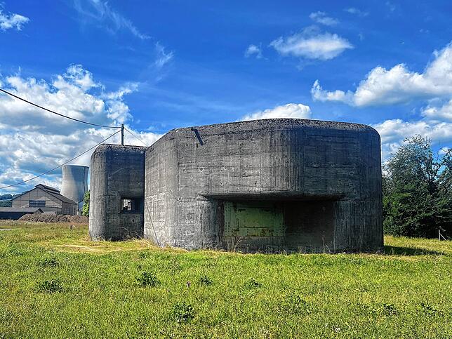 Der Infanteriebunker Fullfeld-West auf einer grünen Wiese vor blauem Himmel. Im Hintergrund das Kernkraftwerk Leibstadt. Er war Teil des ...