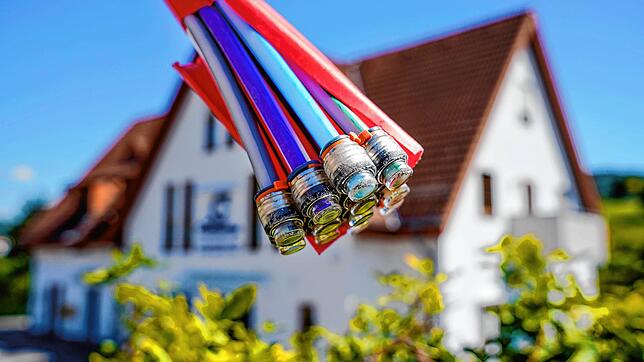 Ein Bündel mit Umhüllungen für Glasfaserkabel hängt vor einem Wohnhaus. (Symbolbild)