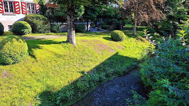 Im Vordergrund die ruhig dahinplätschernde Deggenhauser Aach und im Hintergrund die Terrasse und der Biergarten des Landhotels Adler in ...