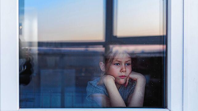 Ein Kind blickt allein aus einem Fenster (Symbolbild). Eine Einzelisolation von Kindern unter 14 Jahren in Quarantäne lehnen die ...