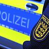 Das Logo der Polizei auf der Dienstkleidung eines Polizisten vor einem Polizeifahrzeug.