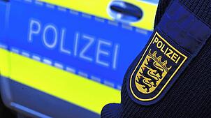 Das Logo der Polizei auf der Dienstkleidung eines Polizisten vor einem Polizeifahrzeug.