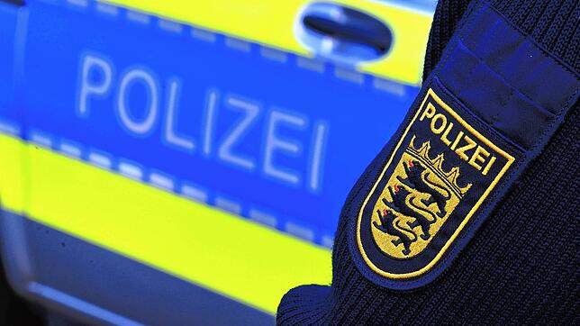 Das Logo der Polizei auf der Dienstkleidung eines Polizisten vor einem Polizeifahrzeug.