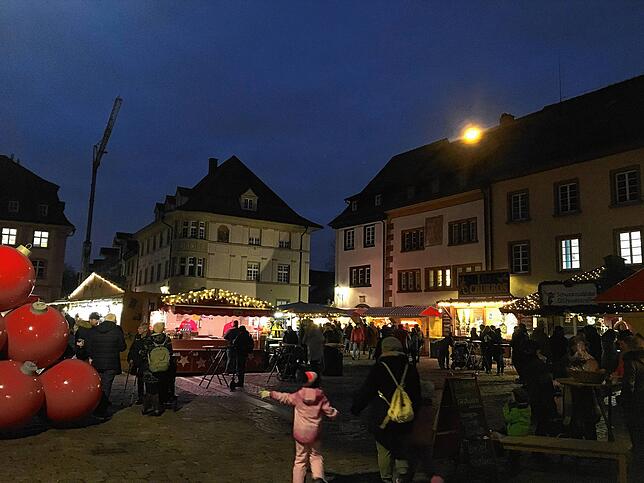 Ein kleines Kind zeigt auf große rote Adventskugeln. Sie sind Teil der Dekoration des Weihnachtsmarktes. Auch bei Dunkelheit wirken sie ...