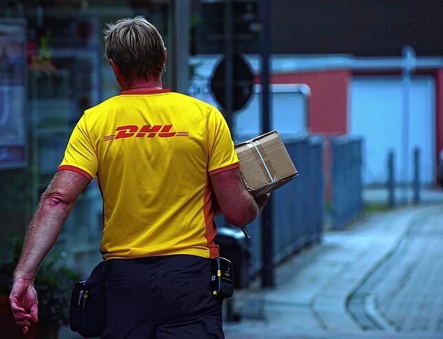Ein Paketzusteller der DHL liefert ein Paket aus. Um die Ausbreitung des Coronavirus zu bremsen, verzichtet das Unternehmen derzeit auf ...