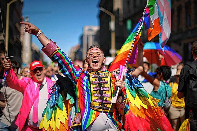 Ein bunt kostümierter Teilnehmer des Pride-Marsches jubelt.