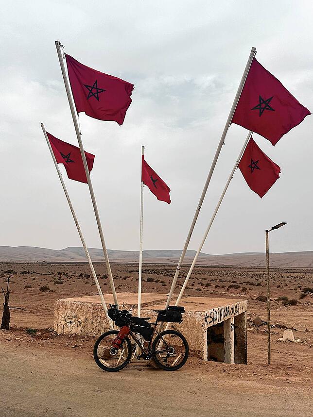 Das Fahrrad von Kauf angelehnt an marokkanischen Flaggen in der Wüste.