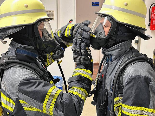 Zwei Feuerwehrler haben die Atemschutzausrüstung angelegt und testen gegenseitig, ob die Maske perfekt sitzt.
