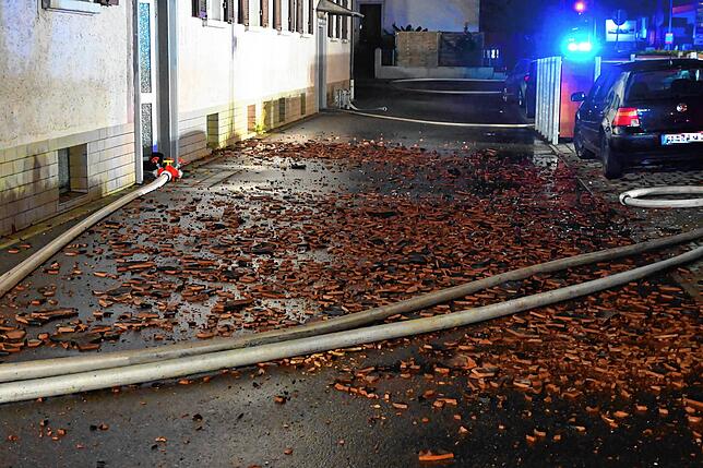 Kaputte Dachziegel liegen vor dem Haus. Die Feuerwehr muss das Dach für die Löscharbeiten öffnen.