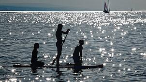 Drei Kinder sind im Bodensee auf einem SUP unterwegs.