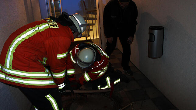 Intensiv bemühen sich die Blumberger Feuerwehrleute, den Schachtdeckel am Hintereingang des Rathauses II zu öffnen, rechts beobachtet ...