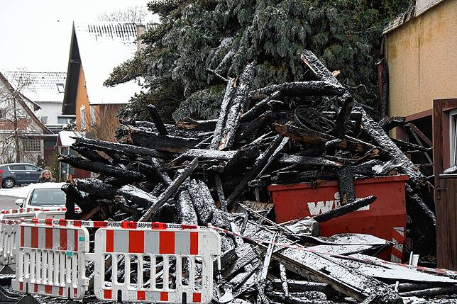 Hinter der Polizeiabsperrung türmt sich verbranntes Gebälk an der Brandruine.