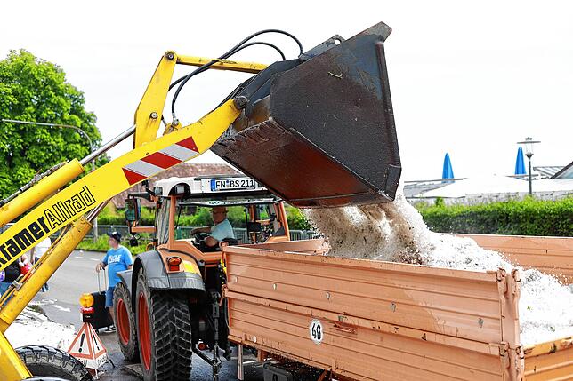 Ein Schaufelradlader der Gemeinde kippt eine Ladung voll Hagel in einen Anhänger, den der Mitarbeiter des Bauhofs in eine Mulde am ...