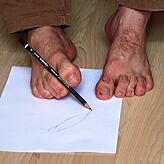Mit den Zehen greift Sebastian Faller den Stift.