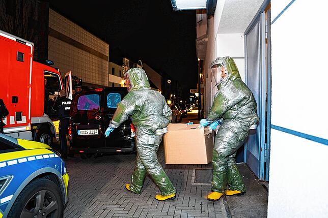 Männer in Schutzanzügen tragen einen Karton aus dem Haus in dem ein Anti-Terror-Einsatz statt fand.